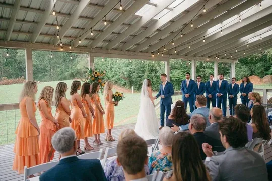Una ceremonia de boda bajo la Grand Veranda techada con luces de bistró y vistas a la granja en las estribaciones de los Smokies
