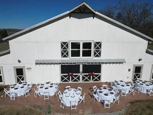 El Grand White Barn con mesas redondas de recepción en el patio frontal, el espacio de recepción para una boda en granja en Tennessee cerca de Sevierville